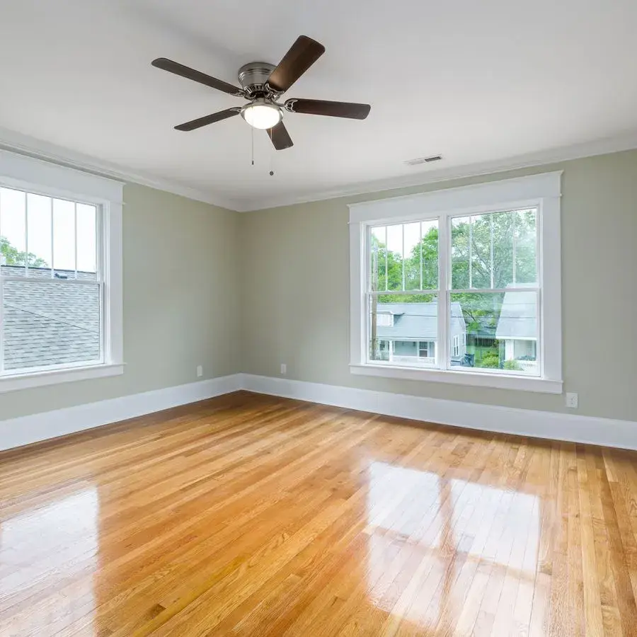 Bright empty room with glossy refinished-look oak hardwood floors, large windows and a ceiling fan