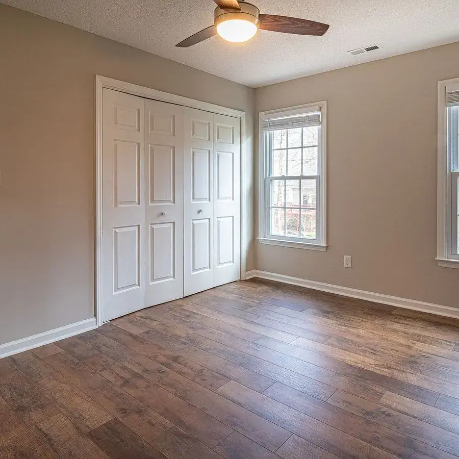 Bedroom with newly installed wood-look plank flooring, white closet doors and a ceiling fan