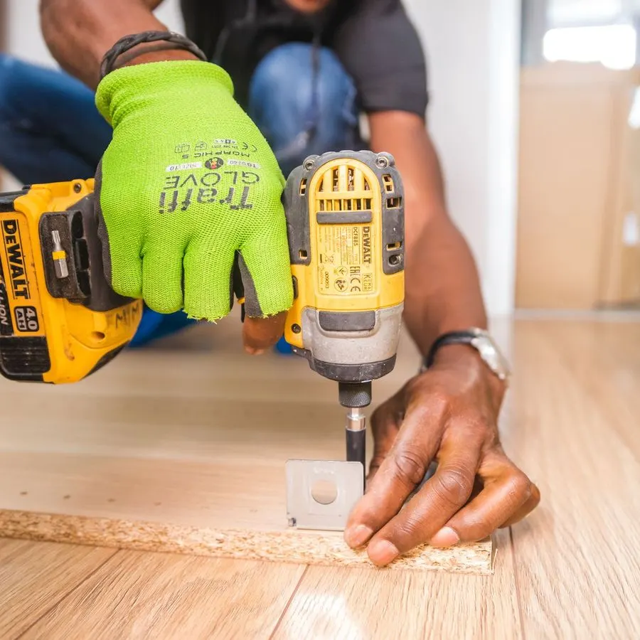 Flooring installer in work gloves using a cordless drill on light wood flooring