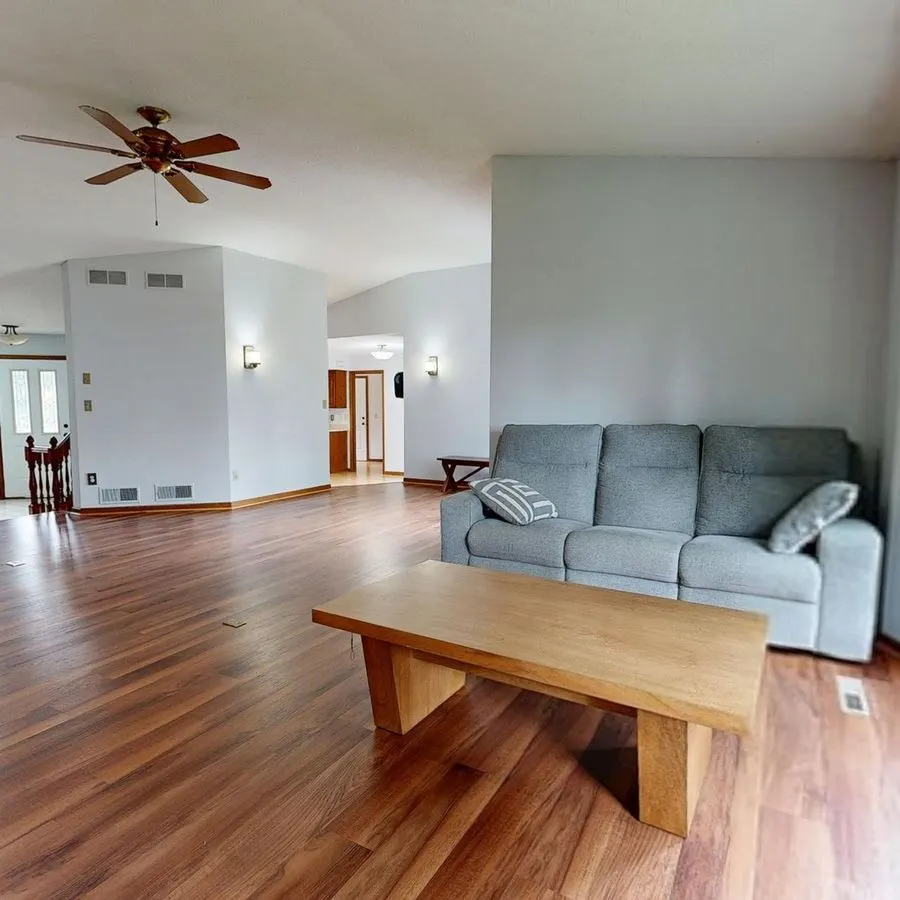 Open living room with rich hardwood floors, a gray sofa and a ceiling fan